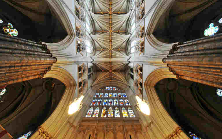The ceiling of Westminster Abbey with stained glass windows and chandeliers hanging down