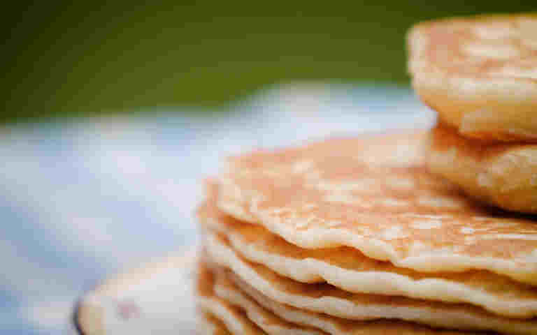 Photograph of a stack of pancakes on a plate, on a table with a blue and white checkered tablecloth within a garden at Westminster Abbey