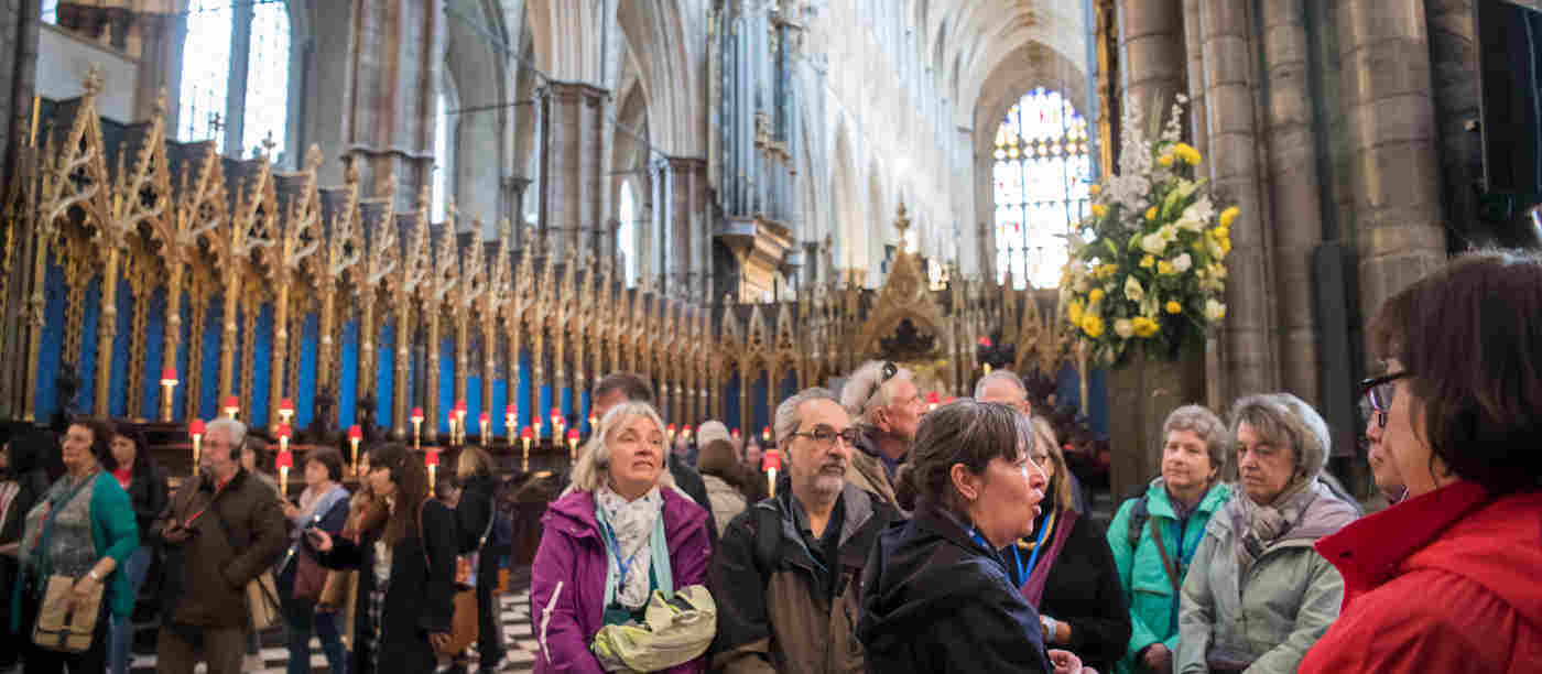 Photograph of a group of visitors listening and looking engaged with their surroundings with a Blue Badge Guide as part of a tour, standing within the crossing of Westminster Abbey