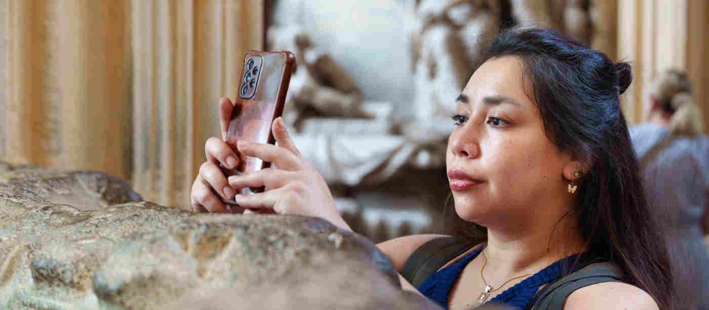 Photograph of member of the public standing next to a stone memorial holding up their phone to take a photograph