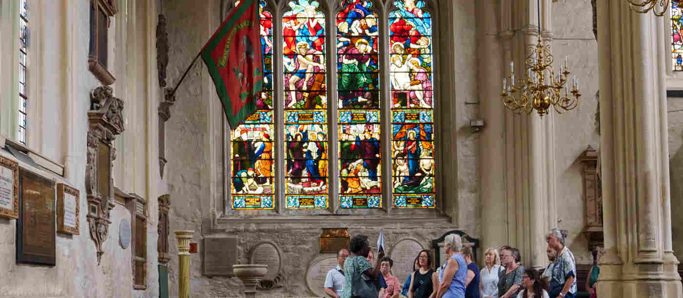 Photograph of tour group within St Margaret's Church next to Westminster Abbey, with a large colourful stained-glass window behind them