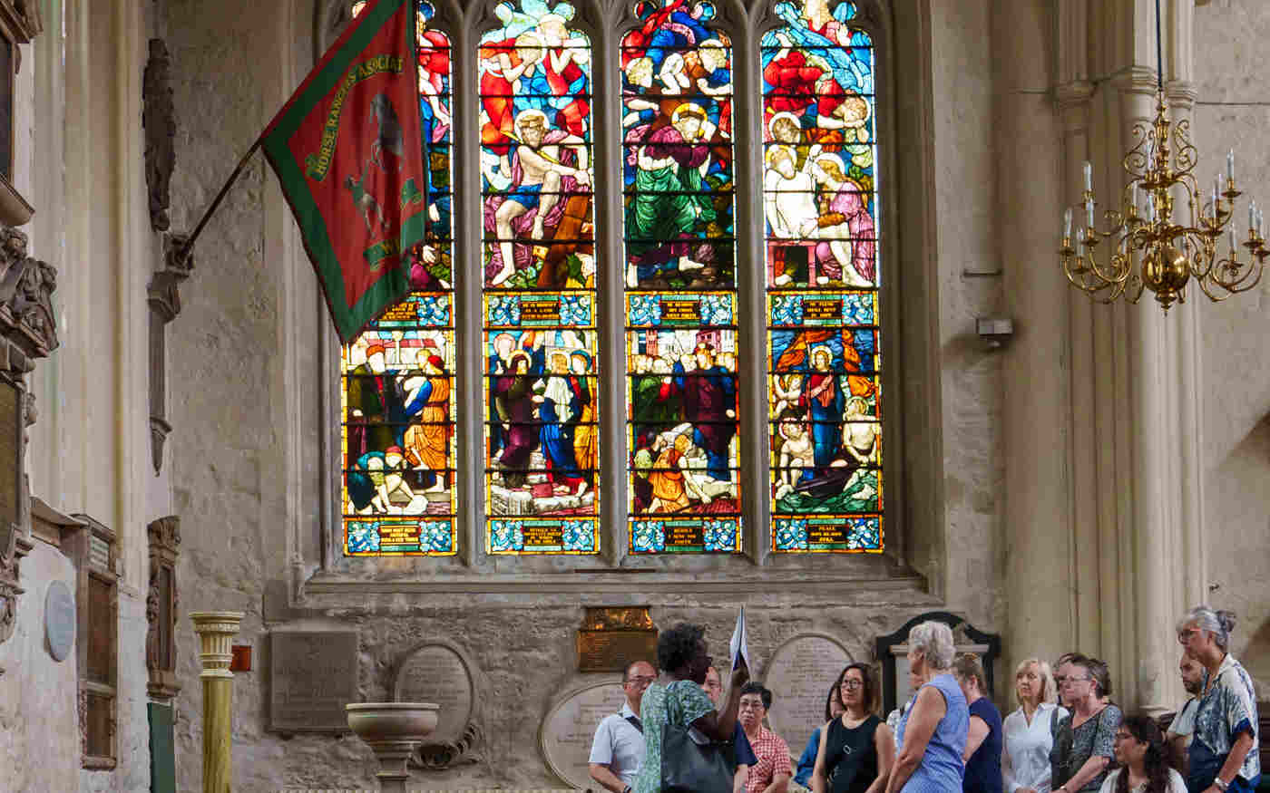 Photograph of tour group within St Margaret's Church next to Westminster Abbey, with a large colourful stained-glass window behind them