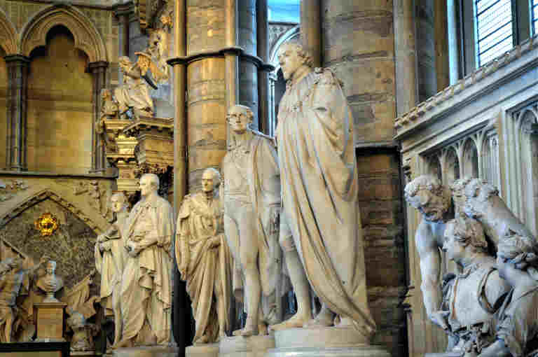 Row of white marble statues of men dressed in ancient Roman-style robes or military uniforms