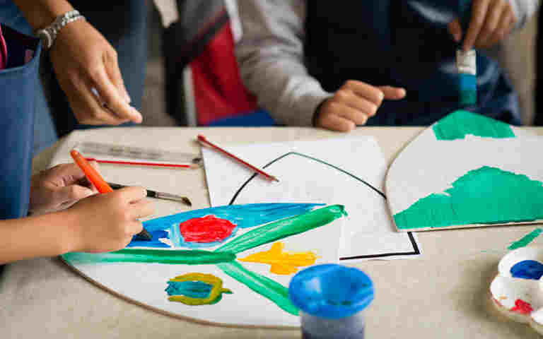 Photograph of adults and children hands creating coats of arms with coloured pens, representing the Coats of Arms Creations template