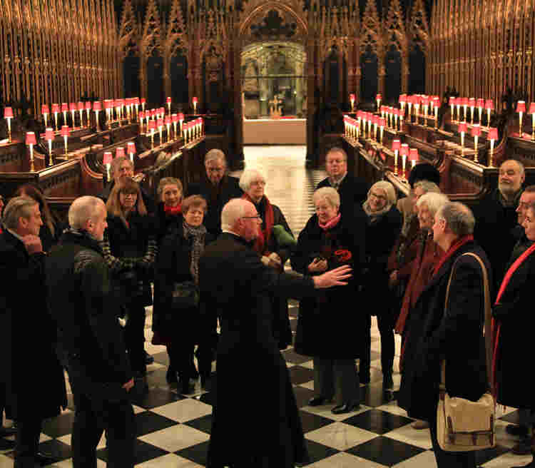 A verger leads a tour group of about 20 people through the Quire of Westminster Abbey
