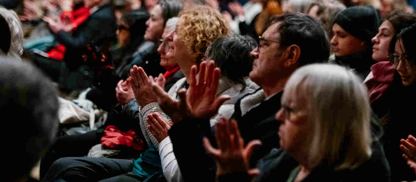 Close-up photograph of a handful of visitors seated and clapping listening to a talk
