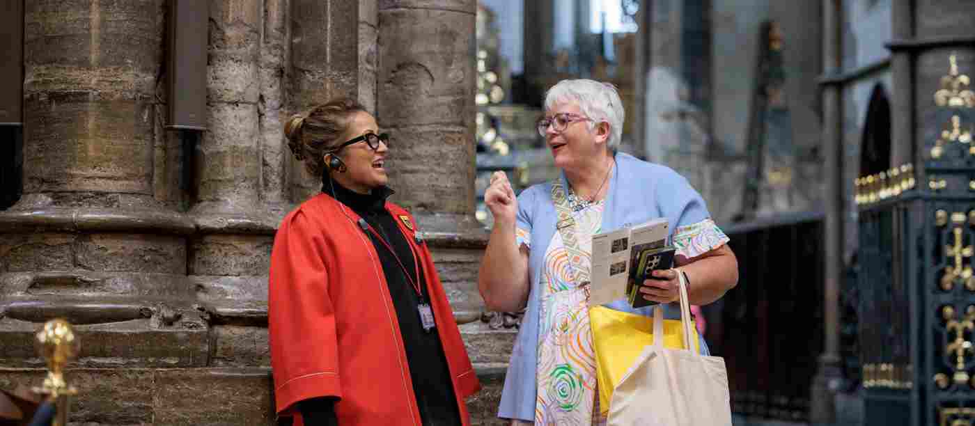 Photograph of member of the public chatting with member of staff wearing a red gown as part of visiting within Westminster Abbey