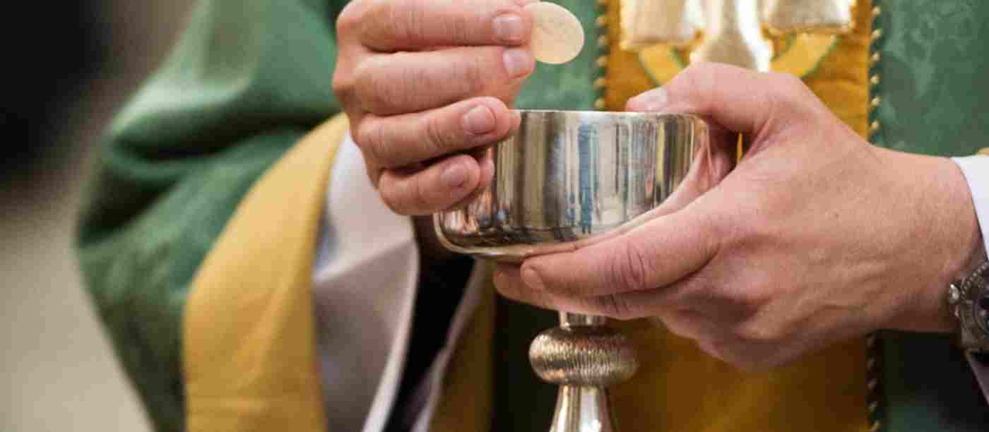 A priest holds a communion wafer and a silver chalice