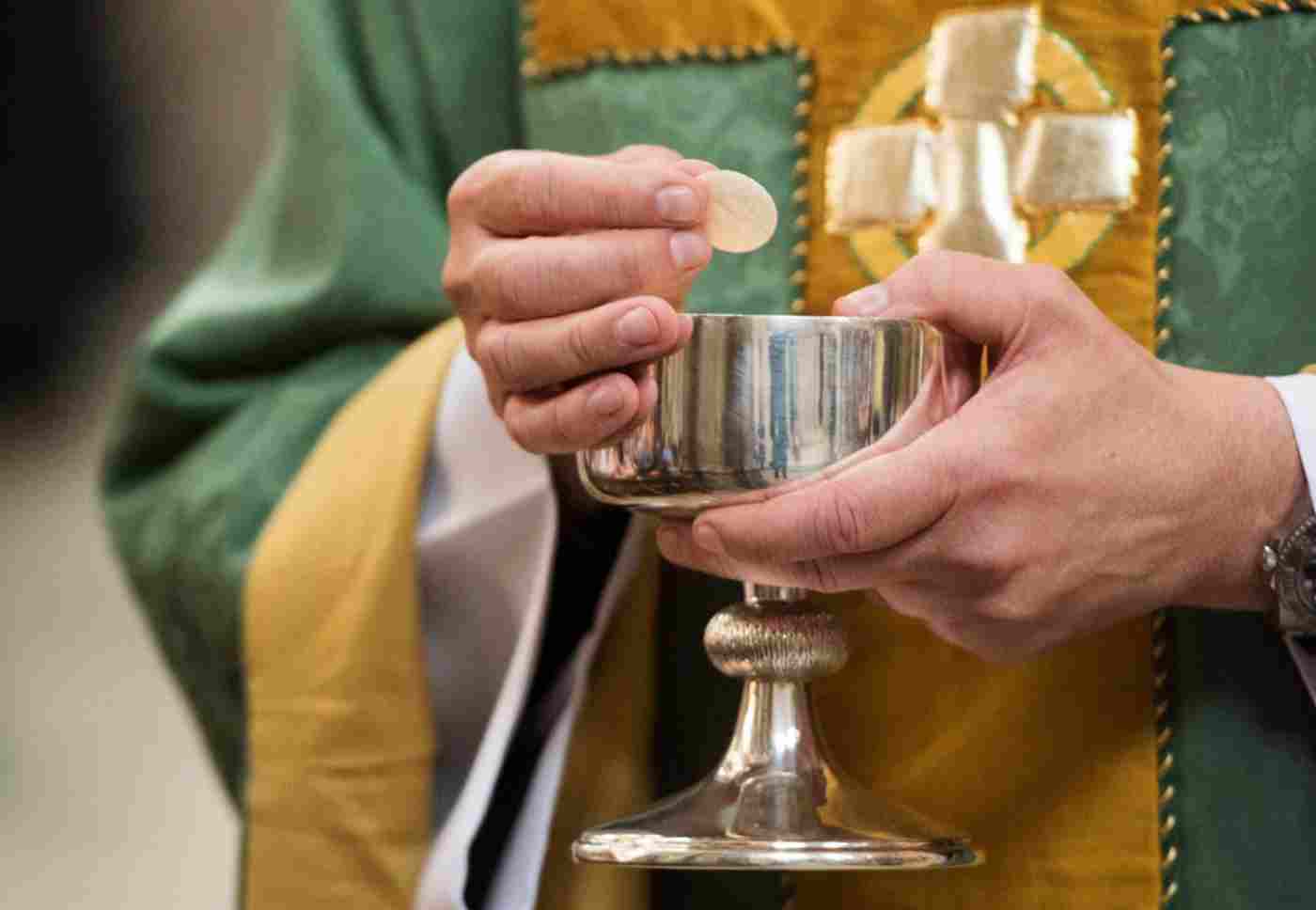 A priest holds a communion wafer and a silver chalice
