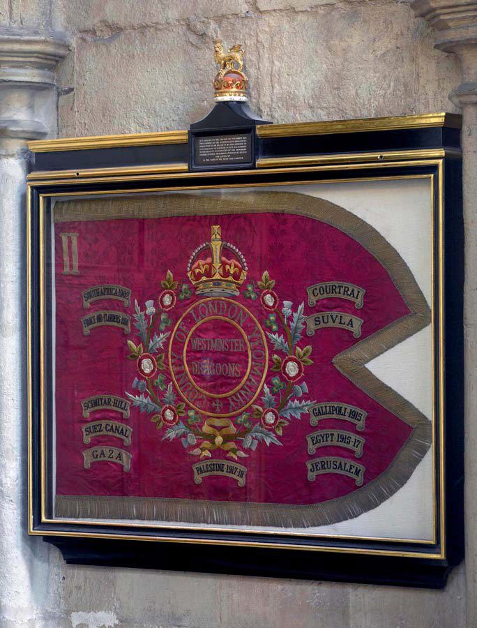 Framed maroon-coloured military flag, fringed with gold, in a frame mounted on the wall