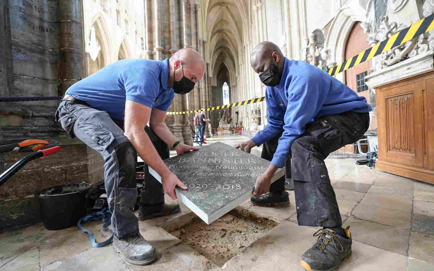 Two men wearing face coverings placing a stone plate into the floor