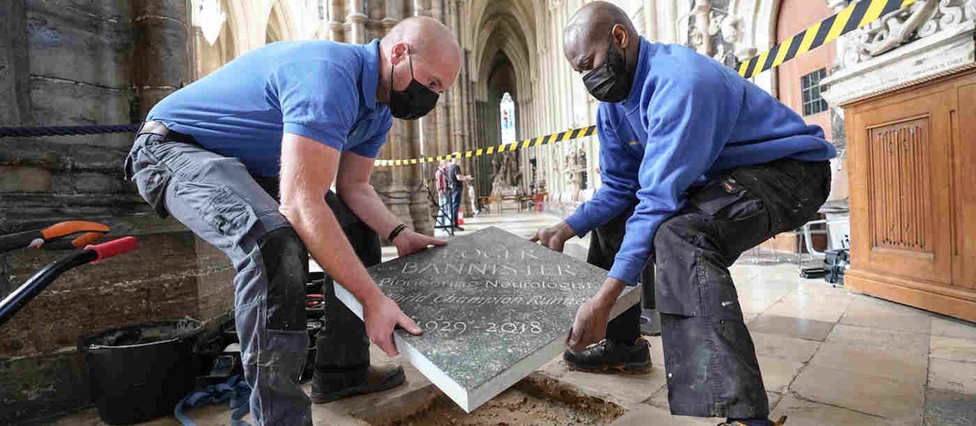 Two men wearing face coverings placing a stone plate into the floor