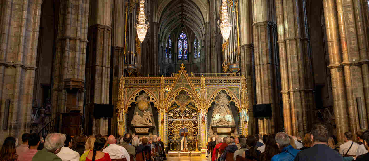 Photograph of a the back of a seated talk with a speaker standing in front of the nave screen within Westminster Abbey