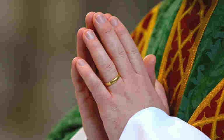 Photograph of a priest praying with their hands together in Westminster Abbey, representing prayer and worship