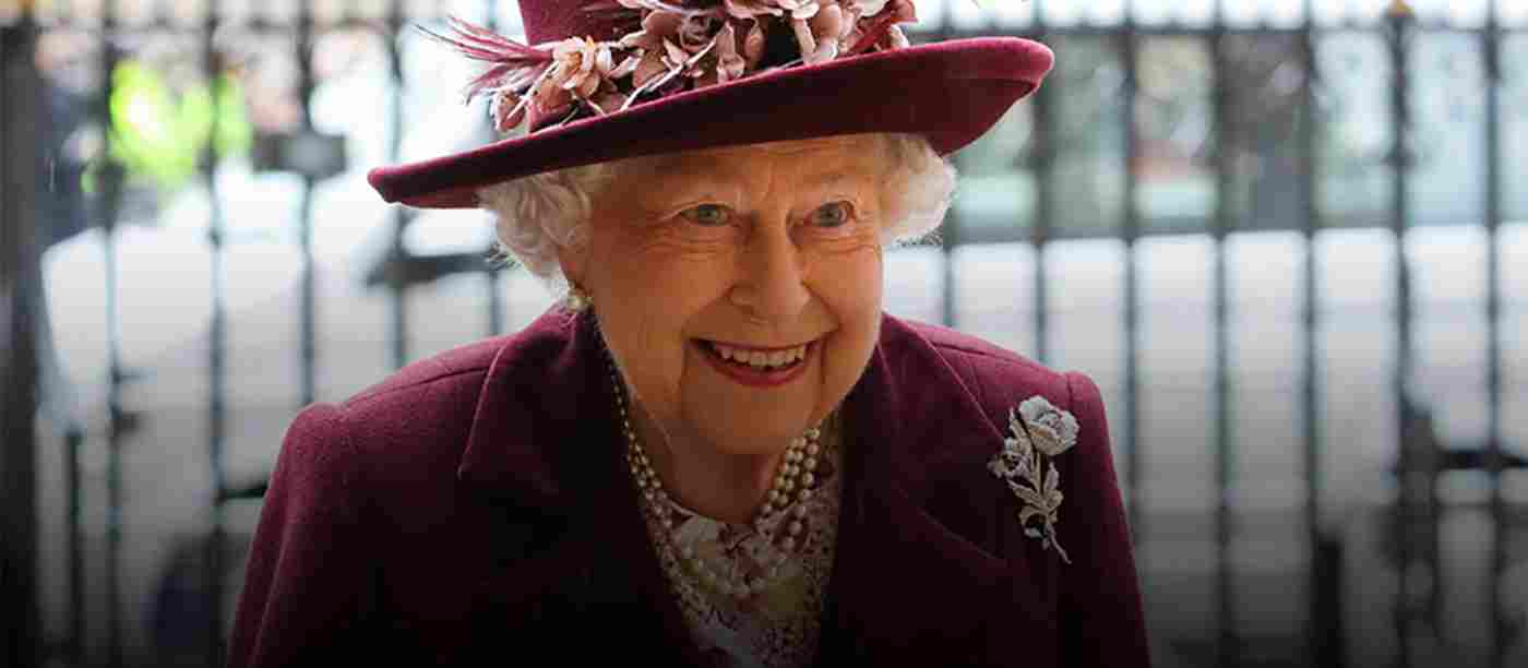 Queen Elizabeth II smiling. She is wearing a burgundy hat and a burgundy jacket
