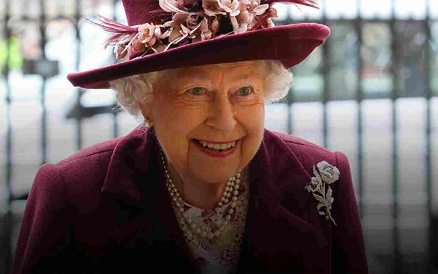 Queen Elizabeth II smiling. She is wearing a burgundy hat and a burgundy jacket