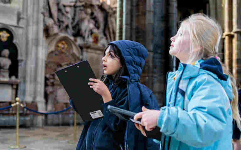 Photograph of two primary students holding clipboards and looking up, representing students using the self-led trails within Westminster Abbey
