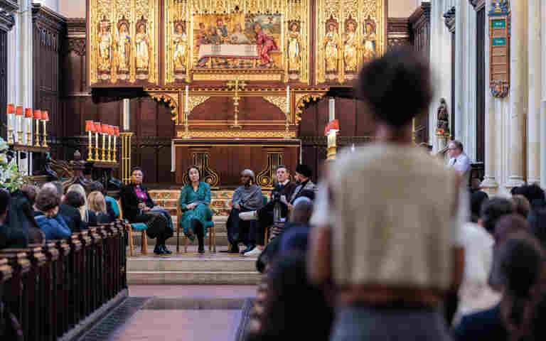 Photograph of the back of a student asking a question with the background of an audience, and a row of panellists at an event in St Margaret's Church