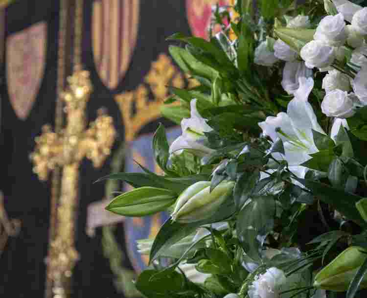 Photograph of funeral flowers with a background of a cross and black alter cloth within Westminster Abbey
