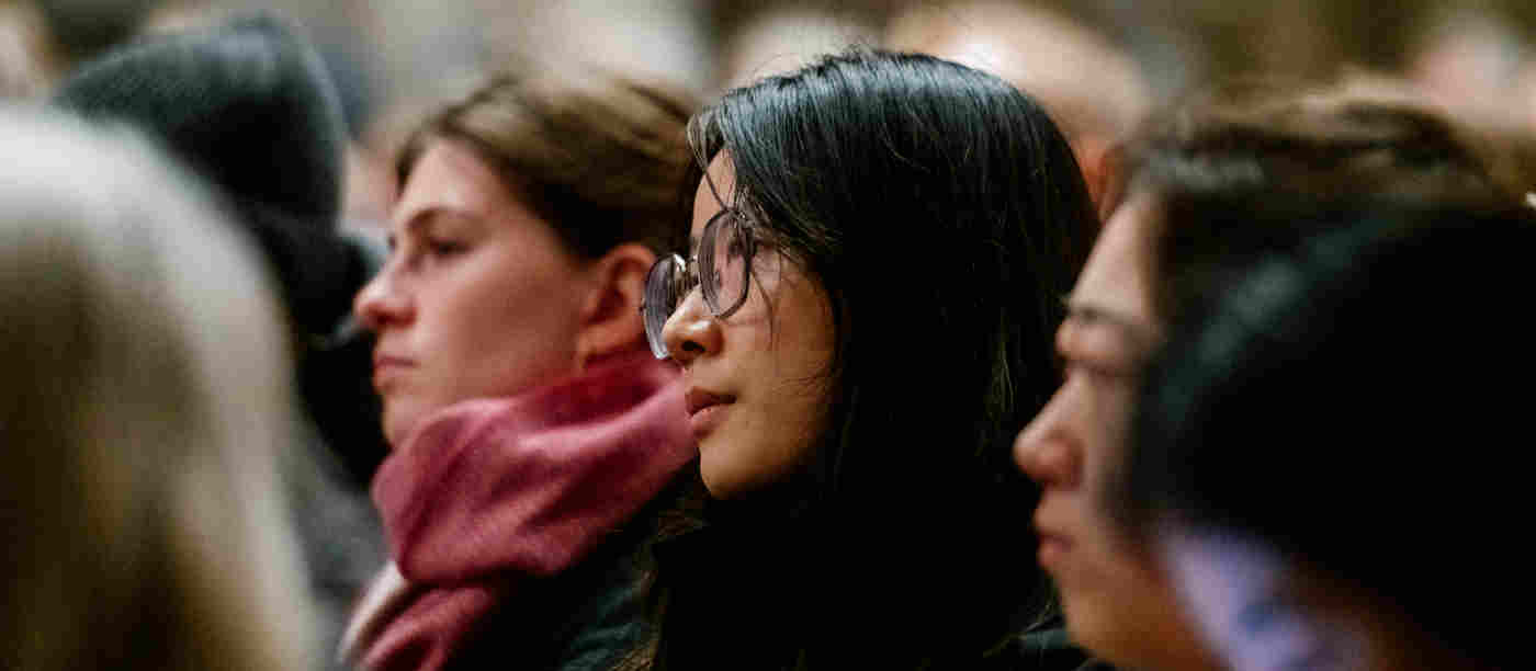 Close-up photograph of woman, with other visitors either sit, listening to a talk