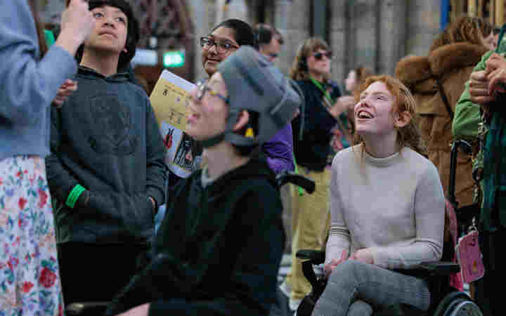 Photograph of young people on a guided tour of Westminster Abbey, some looking up and others looking at a member of staff explaining