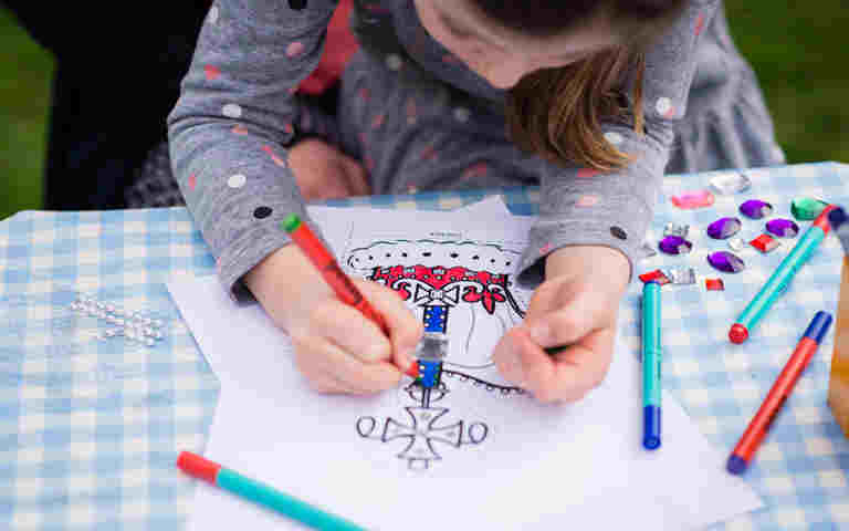 Photograph of young child colouring in a crown template with different coloured felt tip pens, representing What is the Coronation Regalia activity pack