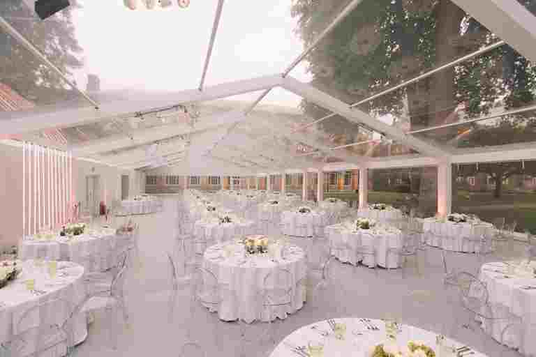 Tables and chairs arranged for a dinner party in a glass marquee in Westminster Abbey's College Garden