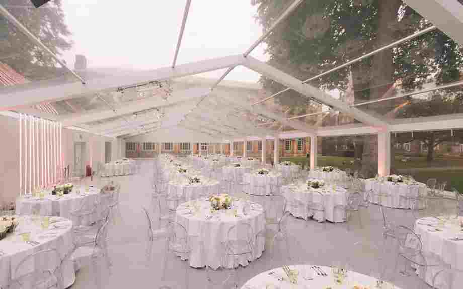 Tables and chairs arranged for a dinner party in a glass marquee in Westminster Abbey's College Garden