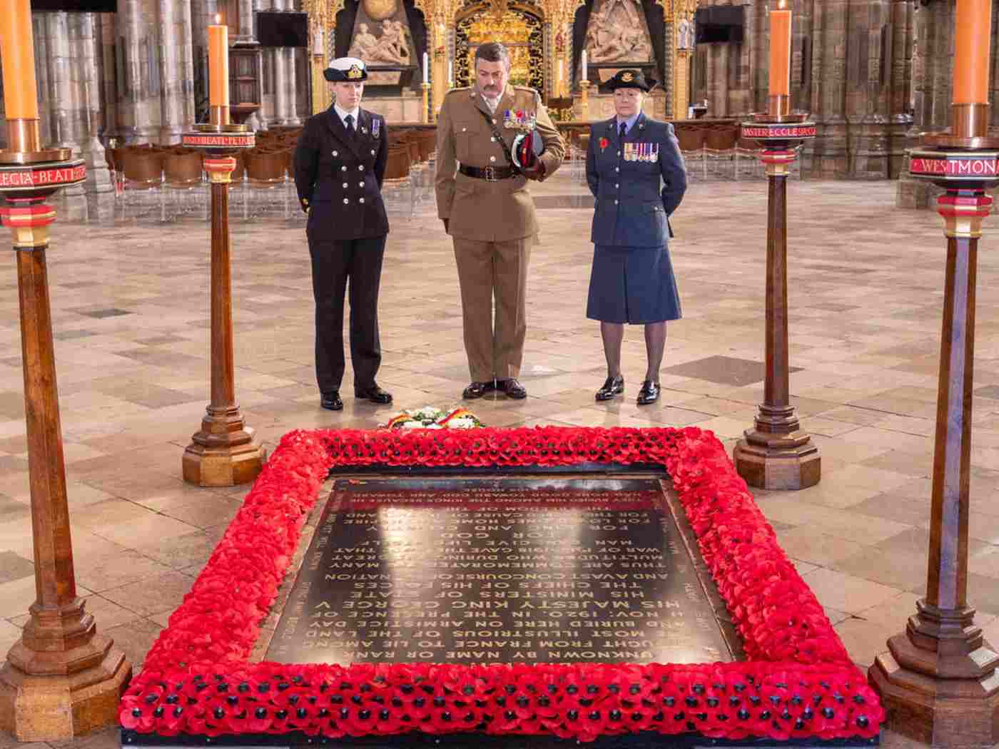A member of the RAF, Royal Navy and the Armed Forces looking at the Grave of the Unknown Warrior (a black marble grave with poppies around the outside)