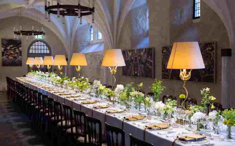 A long table set with lamps, flowers, plates and cutlery for a formal dinner in the Cellarium, Westminster Abbey