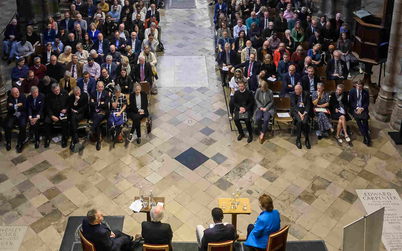 Photograph looking down on a panel of speakers from behind and seeing the front of audience members in the nave of Westminster Abbey