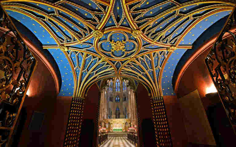 Photograph looking through the quire towards the High Altar of Westminster Abbey, with the top half of the image taken up by the blue ceiling with gold architectural detail and stars