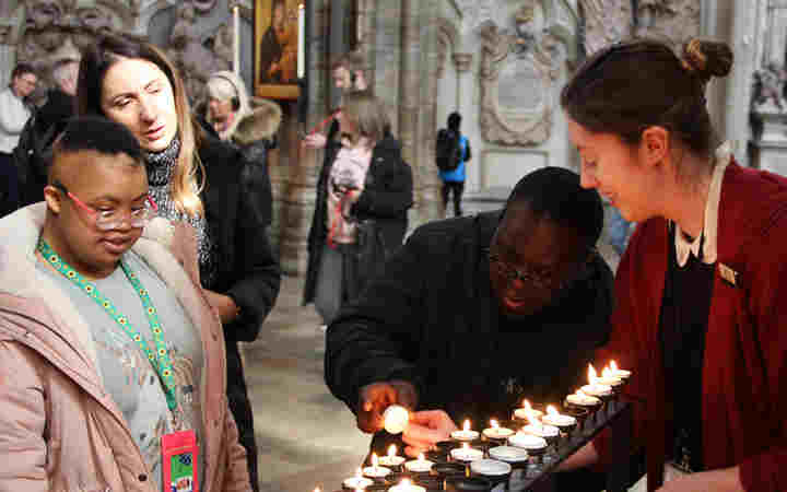 Photograph of young people and a member of staff votive lighting candles within the nave at Westminster Abbey