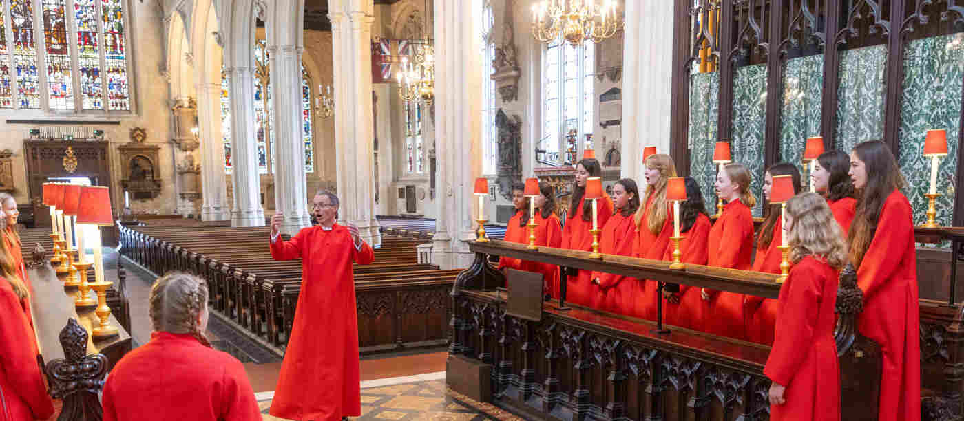 Photograph of female choristers and a male conductor, dressed in red, singing in the choir in St Margaret's Church