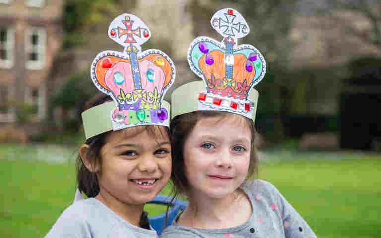 Photograph of two children wearing their crowns in the garden of Westminster Abbey, representing the coronation crowns video