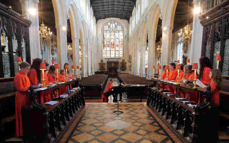 Photograph of St Margaret's Choristers rehearsing, wearing red robes in St Margaret's Church, Westminster Abbey, looking from altar down the church