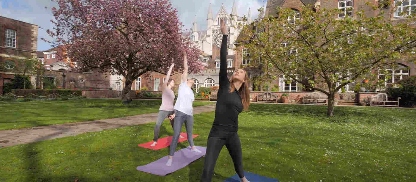 Photograph of three women in yoga poses within College Garden at Westminster Abbey