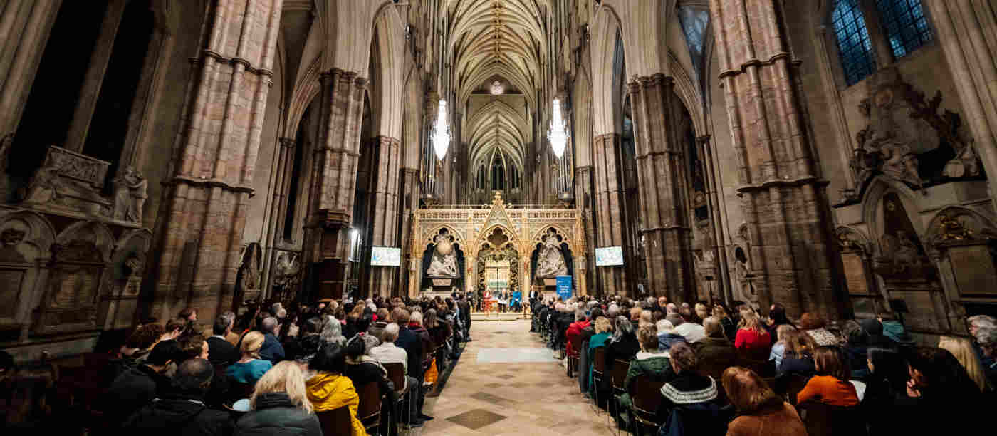 Photograph showing the backs of the audience attending a panel discussion, sitting within the Nave of Westminster Abbey