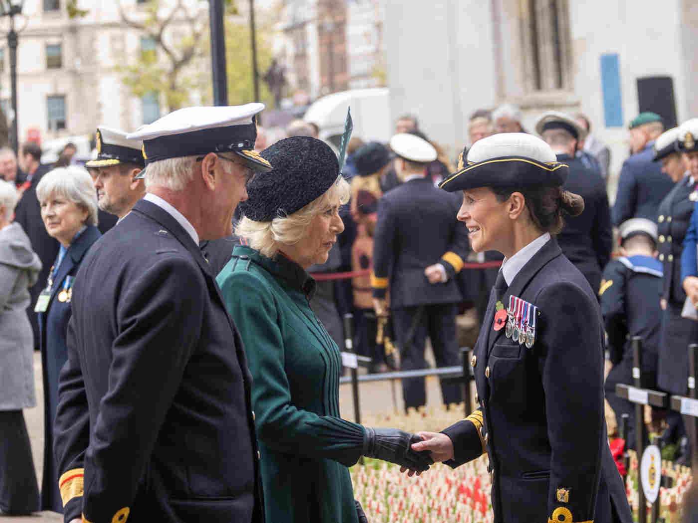The Queen Consort shakes hands with a member of the Armed Forces. Other members of the Armed Forces and poppies are in the background