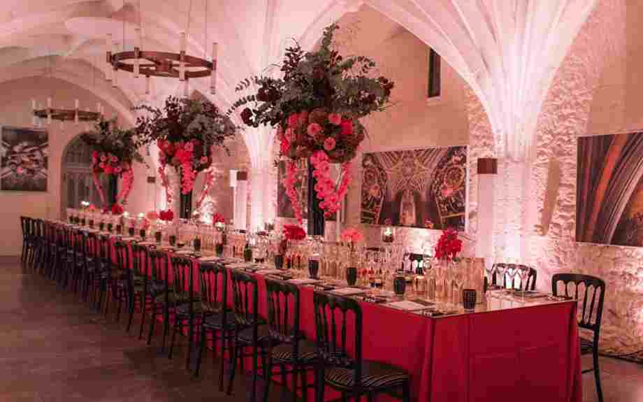 Setting for a formal dinner in the Cellarium, Westminster Abbey, with red tablecloth and flowers