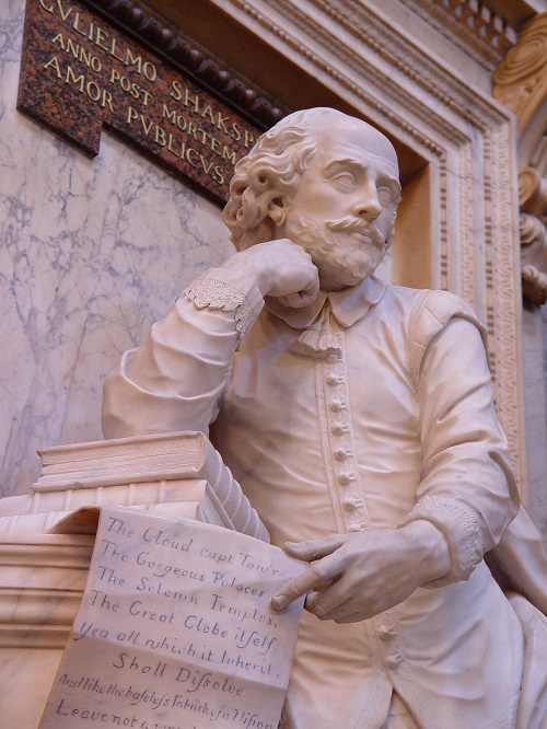 Statue of William Shakespeare, holding a piece of paper with a sonnet on it and leaning on a pile of books