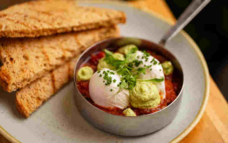 Poached eggs with smashed avocado in a red salsa next to toast