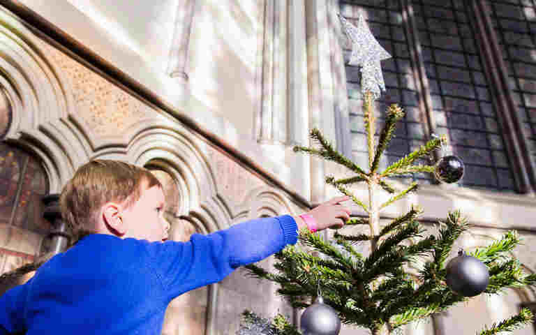 Photograph of child pointing at an ornament on a Christmas tree, representing Christmas celebrations