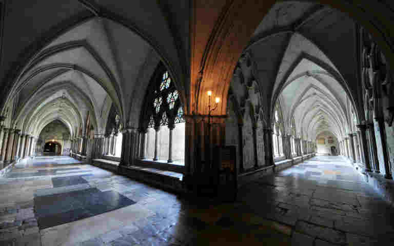 An intersection of two parts of the Cloisters showing arched roofing, paving stones and numerous graves and memorials