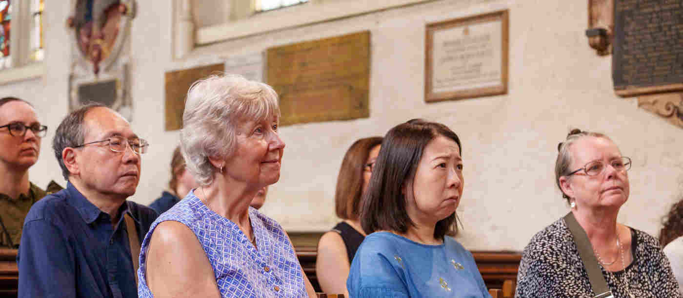 Photograph of a group of visitors sitting listening to a talk within St Margaret's Church, Westminster Abbey