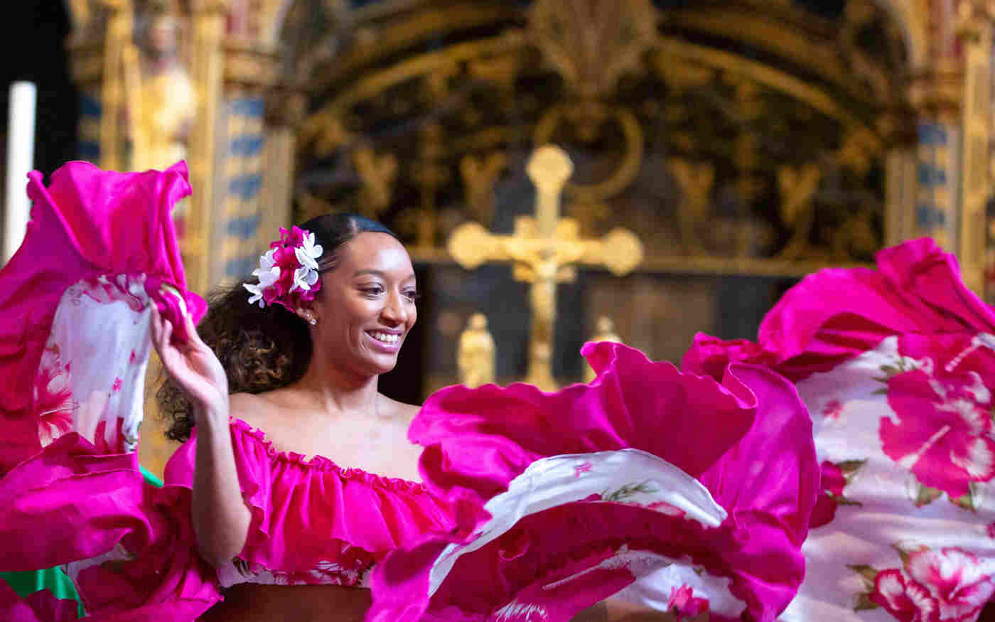 A smiling woman in a pink dress in front of an Altar